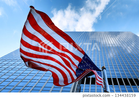 American Flag waves in front of tall building under blue sky American Flag waves in front of tall building under blue sky 134438159