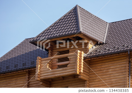 Close-up detail of new modern wooden warm ecological cottage house top with shingled brown roof and wooden sidings on blue sky background. Professionally done carpentry and construction work. 134438385