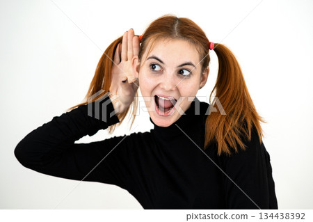 Close up portrait of pretty redhead teenage girl holding a hand to her ear listening to a secret. Close up portrait of pretty redhead teenage girl holding a hand to her ear listening to a secret. 134438392