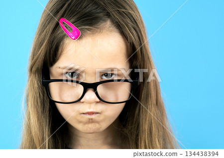 Close up portrait of angry displeased child school girl wearing looking glasses isolated on blue background. Close up portrait of angry displeased child school girl wearing looking glasses isolated on blue background. 134438394