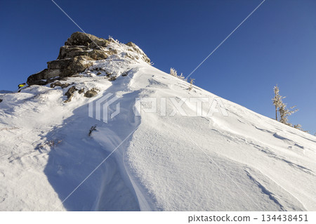Beautiful winter landscape. Steep mountain hill slope with white deep snow, distant woody mountain range panorama stretching to horizon and bright shining sun rays on blue sky copy space background. Beautiful winter landscape. Steep mountain hill slope with white deep snow, distant woody mountain range panorama stretching to horizon and bright shining sun rays on blue sky copy space background. 134438451