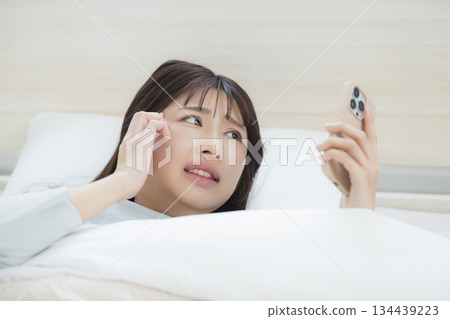 一名婦女在床上的看一個智能手機 一名婦女在床上的看一個智能手機 134439223