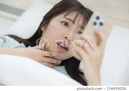 一名婦女在床上的看一個智能手機 134439226