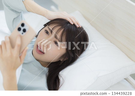 一名婦女在床上的看一個智能手機 一名婦女在床上的看一個智能手機 134439228
