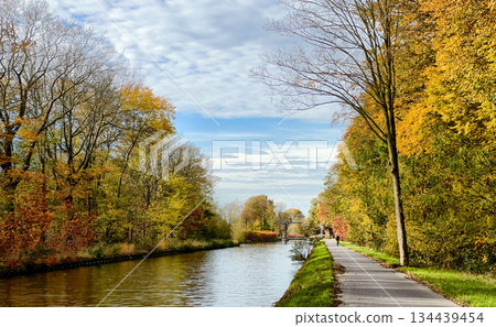 Autumn scenic pathway, Reflective water alongside vibrant fall foliage Autumn scenic pathway, Reflective water alongside vibrant fall foliage 134439454