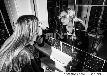 Drunken woman touching her face, looking at her reflection in a bathroom mirror Drunken woman touching her face, looking at her reflection in a bathroom mirror 134439970