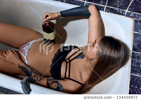 Drunk Woman Sleeping in Bathtub with Bottle of Alcogol Drunk Woman Sleeping in Bathtub with Bottle of Alcogol 134439972