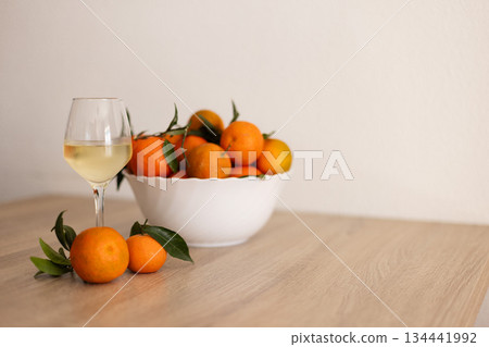 A glass of cold white wine next to tangerines on the wooden table. A glass of cold white wine next to tangerines on the wooden table. 134441992