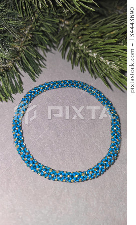 A blue handmade bracelet made of beads and glass beads on a light background. A blue handmade bracelet made of beads and glass beads on a light background. 134443690