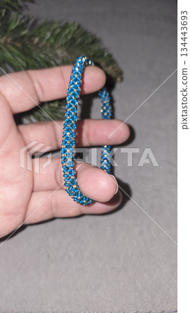 A blue handmade bracelet made of beads and glass beads on a light background. 134443693