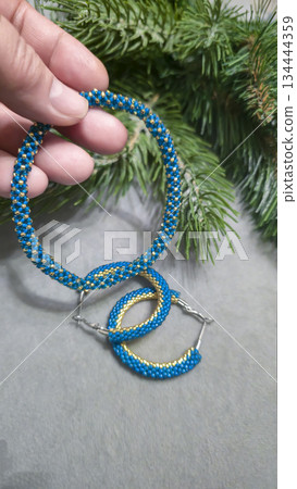 A blue handmade bracelet made of beads and glass beads on a light background. A blue handmade bracelet made of beads and glass beads on a light background. 134444359