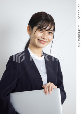 年輕的女商人手持筆記型電腦，在白色背景前微笑。 134445262