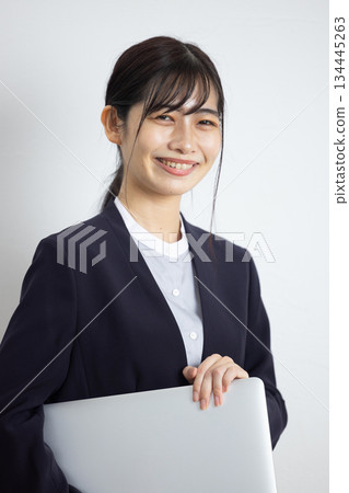 年輕的女商人手持筆記型電腦，在白色背景前微笑。 134445263