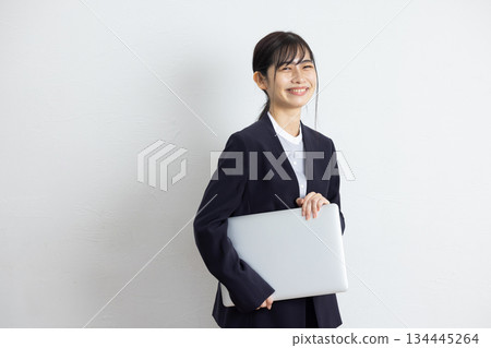 年輕的女商人手持筆記型電腦，在白色背景前微笑。 134445264