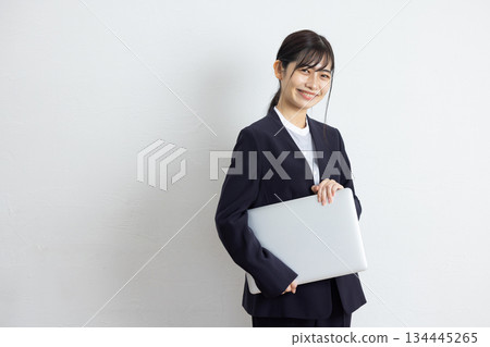 年輕的女商人手持筆記型電腦，在白色背景前微笑。 134445265