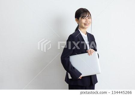 Young businesswoman holding a laptop and smiling in front of a white background Young businesswoman holding a laptop and smiling in front of a white background 134445266