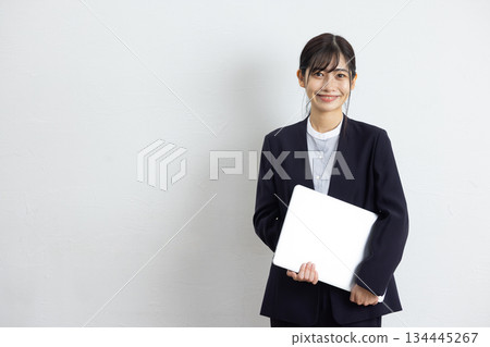 Young businesswoman holding a laptop and smiling in front of a white background Young businesswoman holding a laptop and smiling in front of a white background 134445267