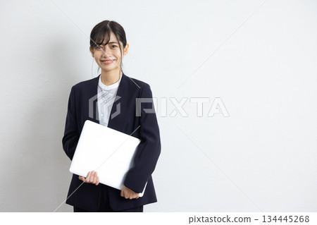年輕的女商人手持筆記型電腦，在白色背景前微笑。 134445268