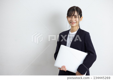 年輕的女商人手持筆記型電腦，在白色背景前微笑。 134445269