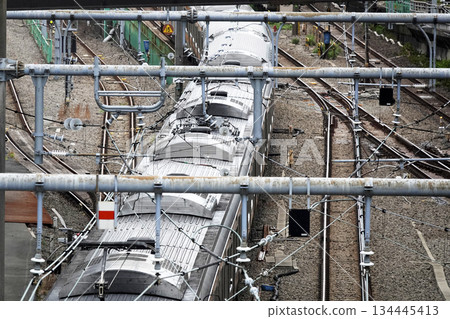 The upper pantograph of a train and overhead wires from an elevated footbridge over the railway line The upper pantograph of a train and overhead wires from an elevated footbridge over the railway line 134445413
