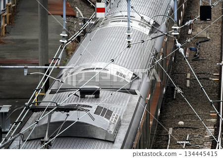 火車的上部受電弓和架設在鐵路線上方高架人行天橋上的架空電線 火車的上部受電弓和架設在鐵路線上方高架人行天橋上的架空電線 134445415
