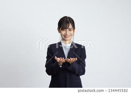 一位年輕的女商人面帶微笑，雙手放在胸前，站在一面白牆前。 134445582
