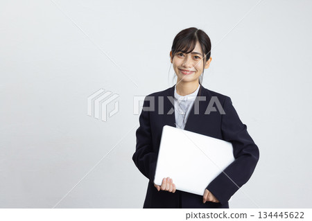 年輕的女商人手持筆記型電腦，在白色背景前微笑。 134445622