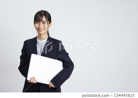 年輕的女商人手持筆記型電腦，在白色背景前微笑。 134445625