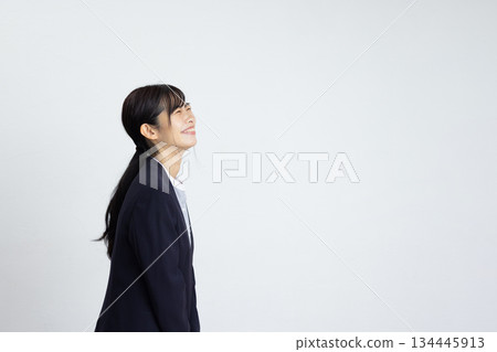 一位年輕女商人站在白牆前，面帶微笑，側臉特寫。 134445913