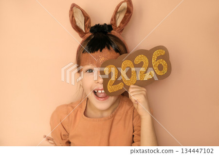A funny girl in a fire horse costume holds the golden numbers 2026. The child is looking forward to the new year with joy and enthusiasm, dressed up as an animal. A funny girl in a fire horse costume holds the golden numbers 2026. The child is looking forward to the new year with joy and enthusiasm, dressed up as an animal. 134447102
