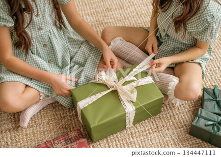 Children open a Christmas gift from Santa wrapped in green paper with a lace bow Children open a Christmas gift from Santa wrapped in green paper with a lace bow 134447111