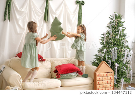 Children are playing and having fun on the couch, throwing each other a pillow in the shape of a Christmas tree Children are playing and having fun on the couch, throwing each other a pillow in the shape of a Christmas tree 134447112