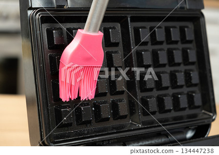Oiling the surface of the waffle iron, preparing for baking homemade waffles. Oiling the surface of the waffle iron, preparing for baking homemade waffles. 134447238