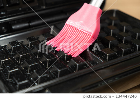 Greasing a waffle iron with a pink silicone brush 134447240