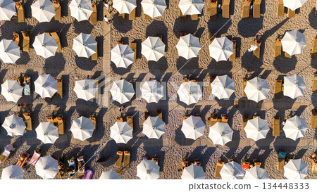 Aerial top view of organized beach umbrellas and sunbeds on a sandy beach. Summer vacation, seaside tourism, leisure and relaxation concept. 134448333