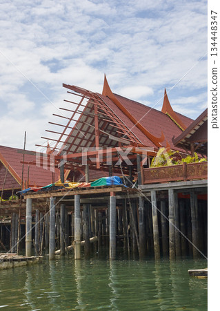 Traditional thai stilt house on water with ornate red roof and blue sky 134448347