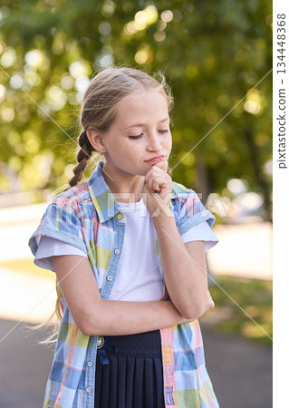 Thoughtful caucasian young girl in colorful shirt outdoors on a sunny day 134448368