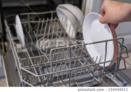 Person loading dishwasher with plates in kitchen setting 134448411