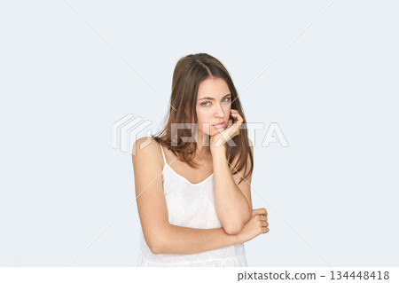 Young caucasian female in white top with hand on face looking pensive against Young caucasian female in white top with hand on face looking pensive against 134448418