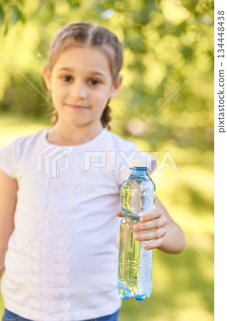 Young caucasian girl holding water bottle outdoors in bright summer day Young caucasian girl holding water bottle outdoors in bright summer day 134448438