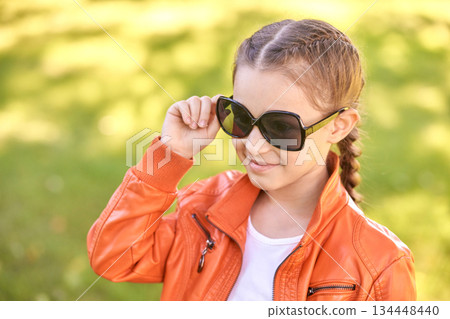 Caucasian young girl in orange jacket and sunglasses outdoors in bright Caucasian young girl in orange jacket and sunglasses outdoors in bright 134448440
