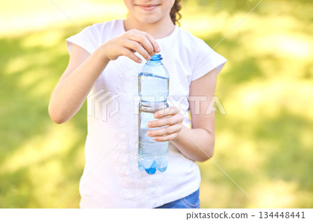 Young caucasian girl holding plastic water bottle outdoors on a sunny day 134448441