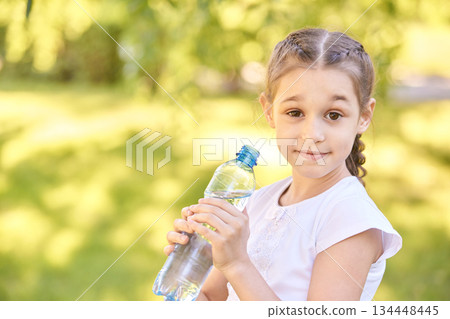 Young caucasian girl holding water bottle in sunny park with green background 134448445