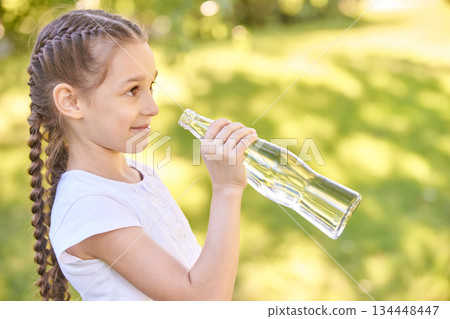 Young caucasian girl with braided hair holding empty glass bottle outdoors 134448447