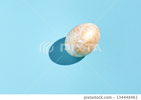 Golden speckled egg on blue background with shadow and marbled texture Golden speckled egg on blue background with shadow and marbled texture 134448461