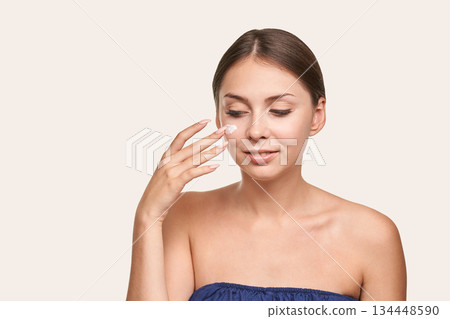 Young caucasian female applying moisturizing cream to face with gentle care Young caucasian female applying moisturizing cream to face with gentle care 134448590