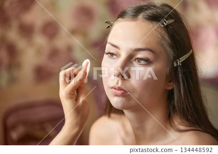 Young caucasian female getting makeup applied with cotton pad by makeup artist Young caucasian female getting makeup applied with cotton pad by makeup artist 134448592