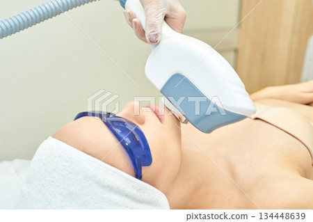 Young caucasian female receiving laser facial treatment in a beauty clinic Young caucasian female receiving laser facial treatment in a beauty clinic 134448639