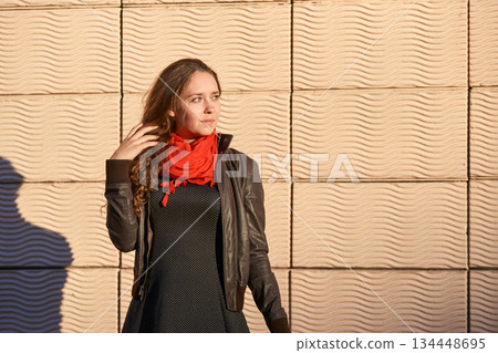 Young caucasian woman in black jacket and red scarf standing against textured Young caucasian woman in black jacket and red scarf standing against textured 134448695