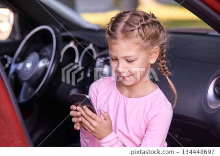 Young caucasian female child with braided hair using smartphone inside car 134448697